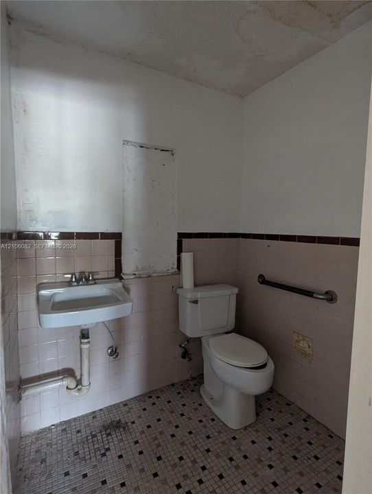Wall-mounted porcelain sink with dual-handle faucet, white vitreous china toilet, ceramic tile wall wainscoting, and patterned floor tiling