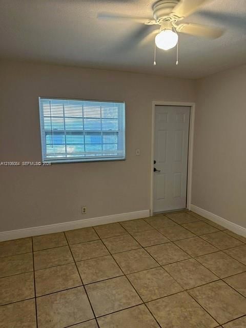 Room featuring neutral wall paint, tile flooring, a horizontal window with blinds, a six-panel door, and a ceiling-mounted light fixture with a fan