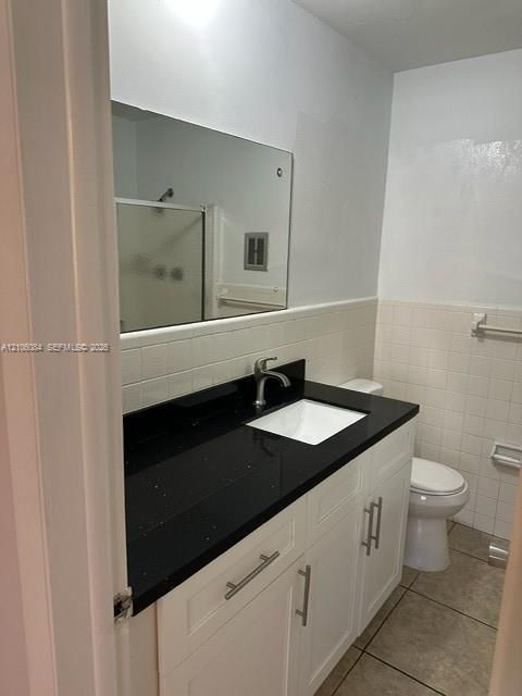 Bathroom vanity featuring a dark stone countertop, integrated rectangular sink, brushed-metal hardware, white cabinetry, and a large frameless mirror
