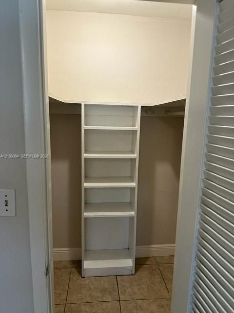 Storage space featuring built-in vertical shelving, a horizontal hanging rod, and tile flooring, secured by a louvered bifold door