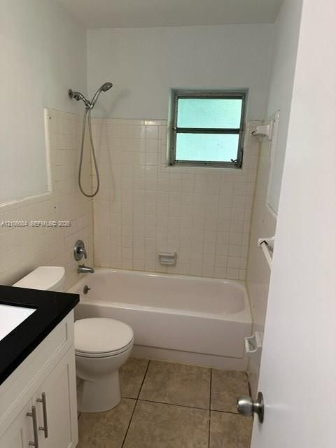 Bathroom featuring a shower and tub combination with wall-surround tiling, a vanity with a dark countertop and white cabinetry, and tile flooring