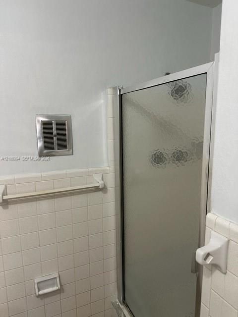 Shower enclosure with textured glass door, white square wall tile, built-in recessed soap dish, and wall-mounted towel bar