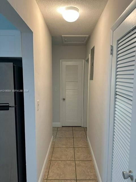 Hallway featuring tile flooring, ceiling-mounted lighting, and louvered-style interior doors