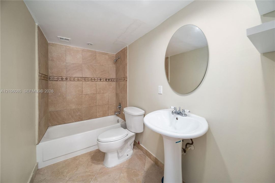 Bathroom featuring a pedestal sink, oval wall-mounted mirror, tiled shower enclosure with decorative inlay, and tile flooring