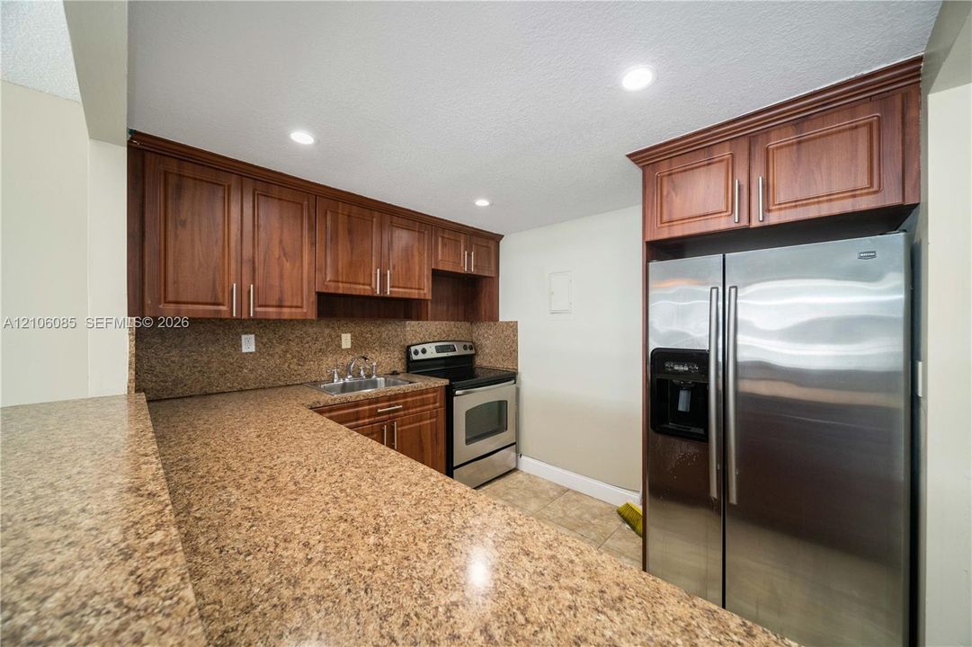 Kitchen featuring wood cabinetry, solid-surface countertops, stainless steel refrigerator, stainless steel range, and tile flooring