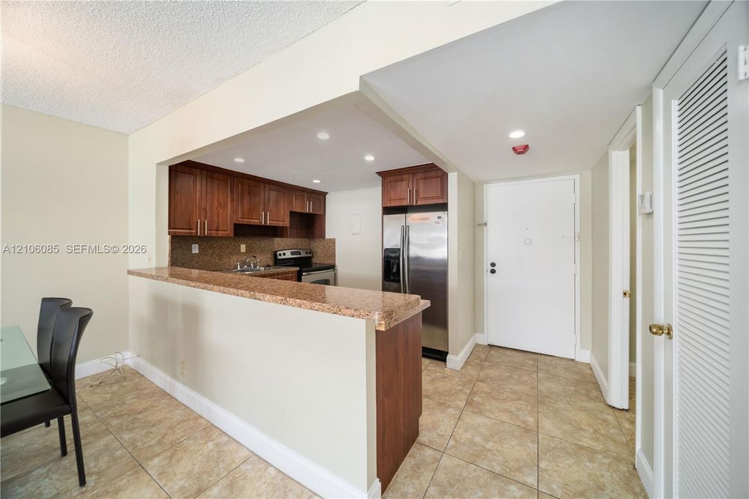 Kitchen featuring wood cabinetry, stone-surface breakfast bar, tile flooring, stainless steel appliances, and recessed lighting