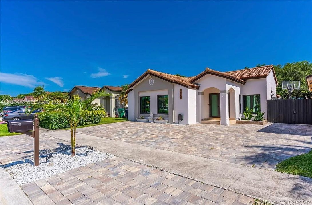 Single-story residence featuring a tile roof, light-toned stucco exterior, arched covered entryway, and an expansive paved driveway