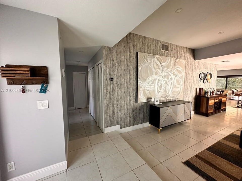 Interior space featuring large-format tile flooring, textured accent wall covering, recessed ceiling lighting, and double-door closet storage