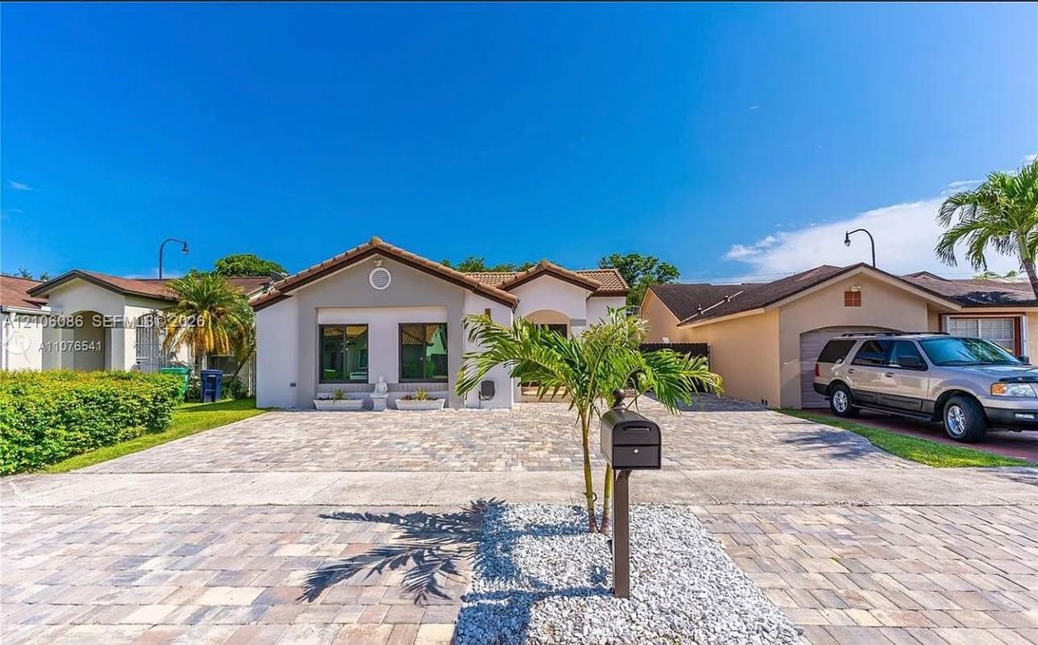 Stucco exterior featuring a tiled gable roof, paver driveway, and an integrated garage