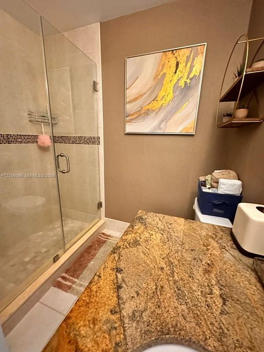 Glass-enclosed shower with tiled walls and a decorative mosaic border, complemented by a stone-surfaced vanity