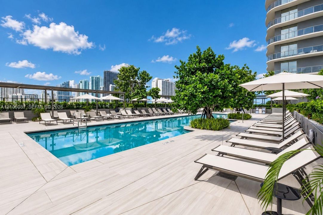 Outdoor swimming pool featuring a tile deck, integrated landscaping, and shaded areas