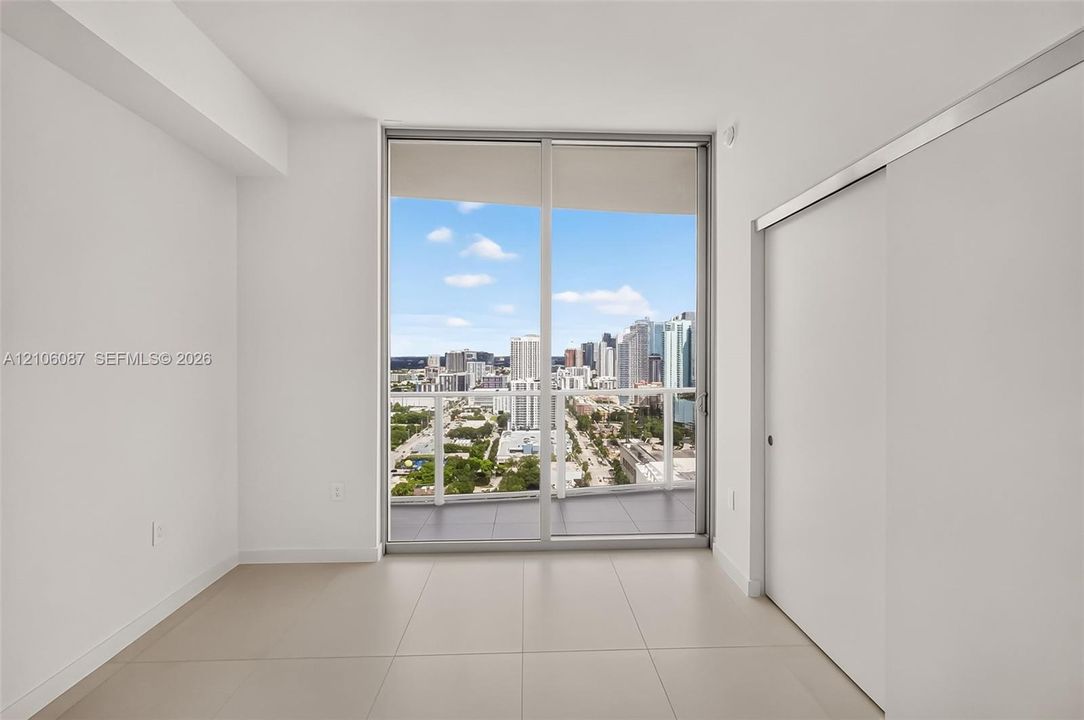 Floor-to-ceiling sliding glass doors, private balcony, neutral large-format tile flooring, and urban skyline backdrop