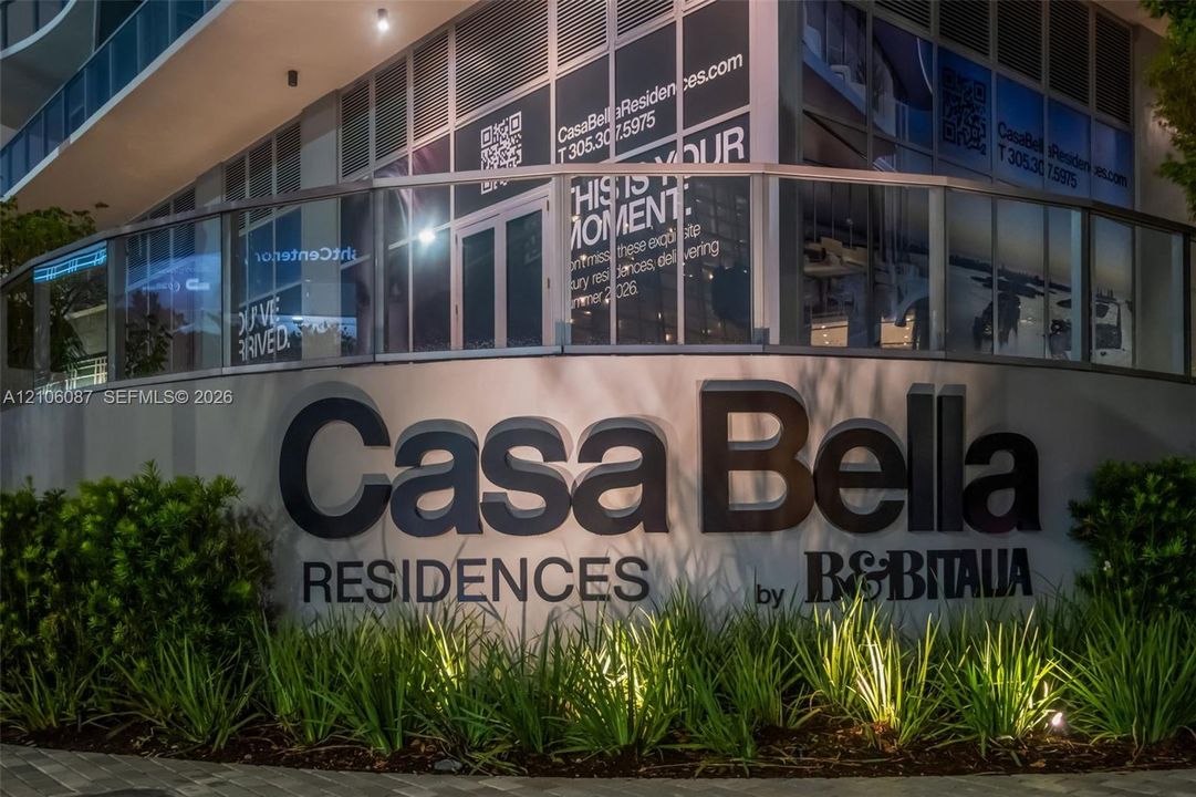 Exterior signage for Casa Bella Residences featuring dimensional lettering, low-profile landscape planting, and glass railing balcony enclosure