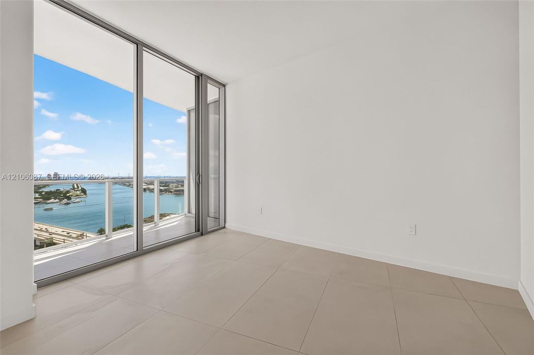 Floor-to-ceiling glass wall, large-format tile flooring, and sliding glass door leading to a balcony with waterfront scenery