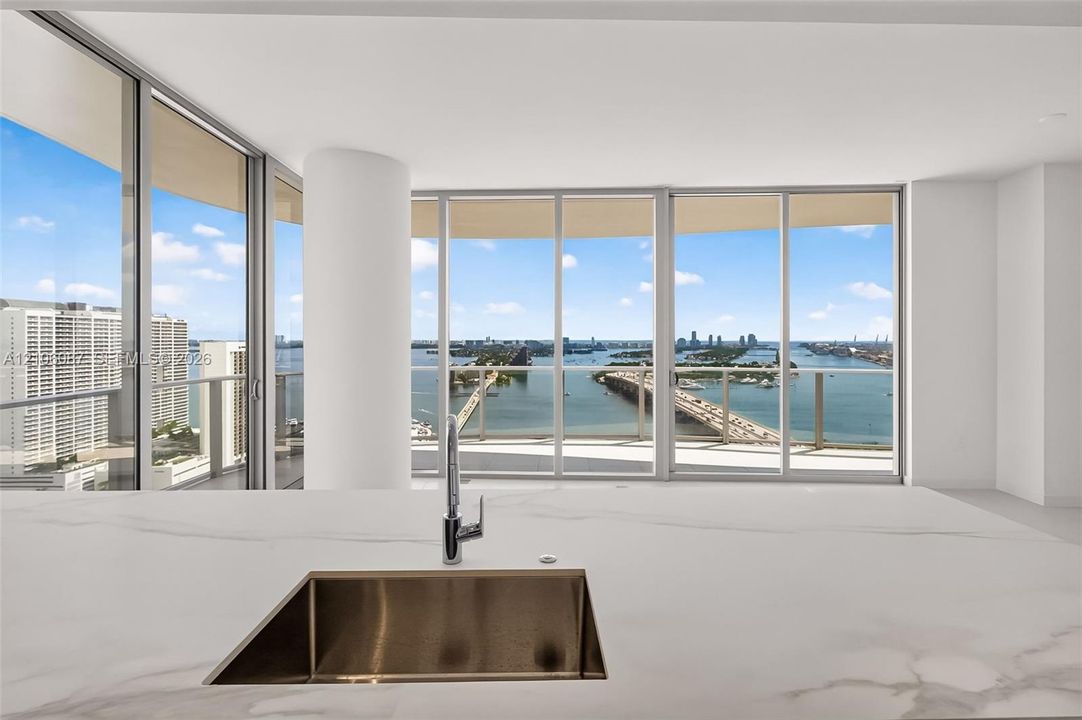 Kitchen featuring a waterfall-edge stone countertop, undermount stainless steel sink, chrome faucet, floor-to-ceiling windows, and access to a balcony
