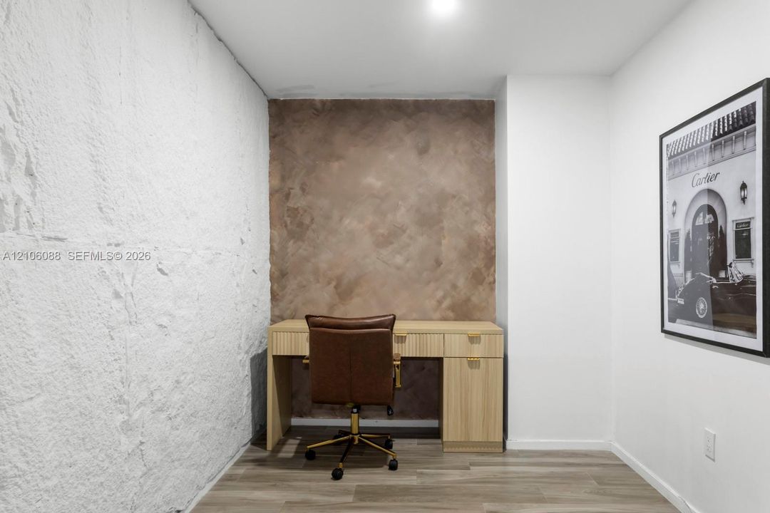 Textured white masonry wall, custom built-in wooden desk with drawers, wood-finish flooring, and a decorative plaster feature wall