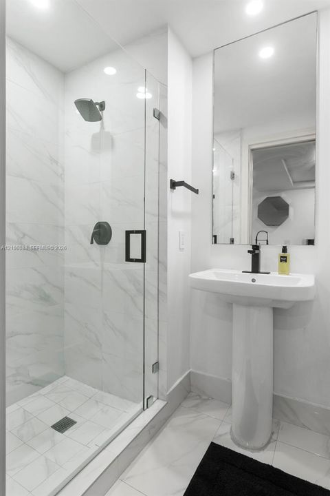 Walk-in shower with floor-to-ceiling veined tile, frameless glass enclosure, matte black fixtures, and a pedestal sink