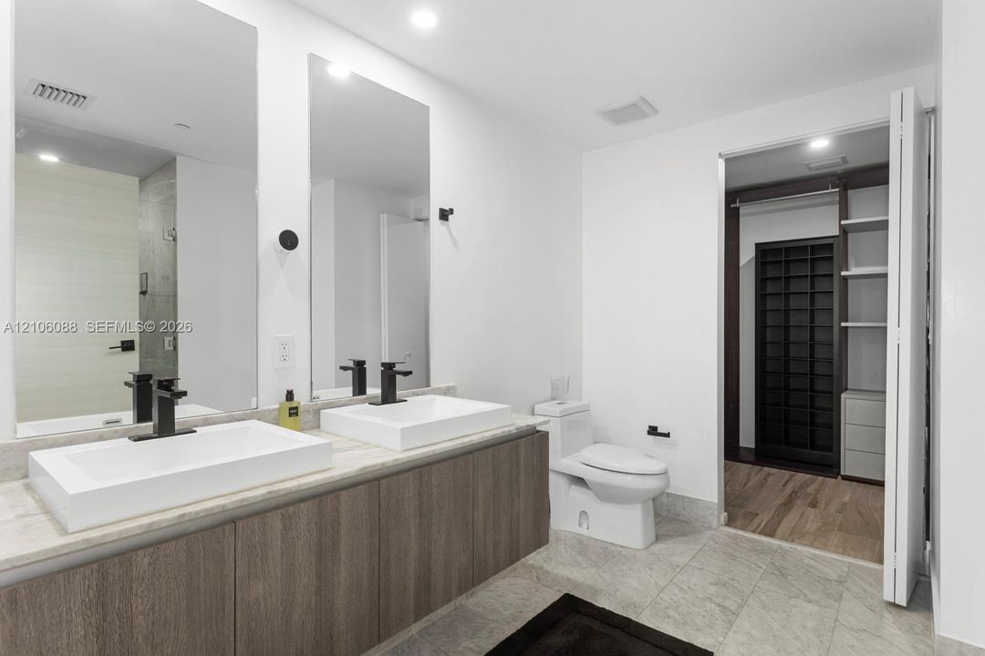 Floating vanity featuring dual rectangular vessel sinks, stone-finish countertops, matte black fixtures, and built-in closet cabinetry