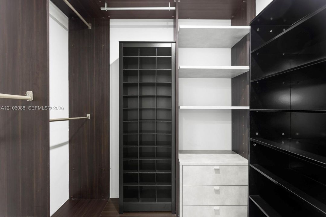 Custom storage system featuring dark wood-finish cabinetry, a built-in shoe rack, three integrated drawers with a stone-finish facade, open shelving, and metal garment rods