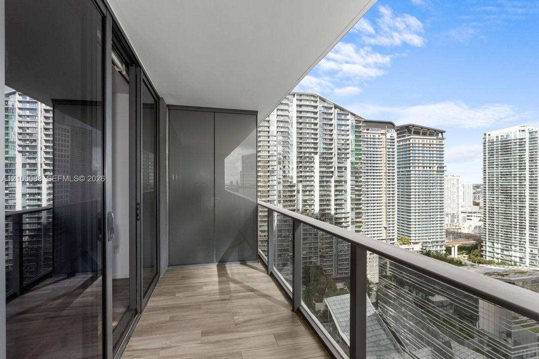 Covered balcony featuring wood-finish flooring, full-height glass sliding doors, and a glass-paneled railing
