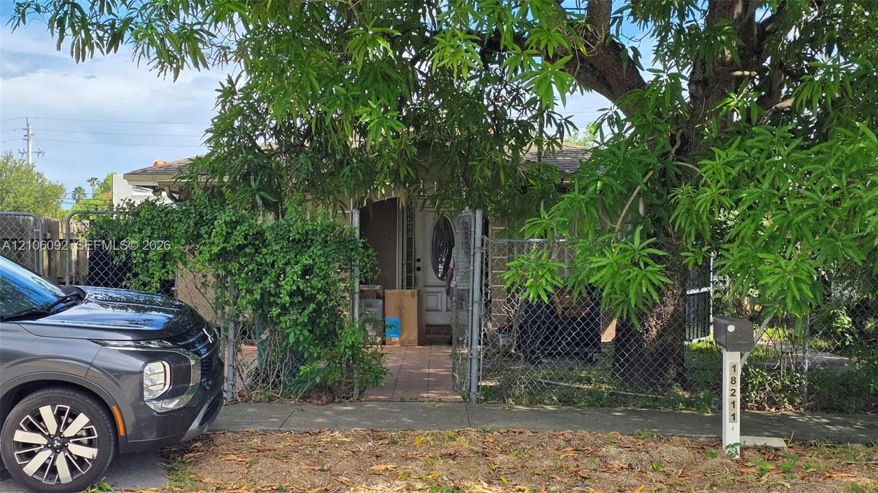 Exterior featuring a masonry facade, tiled entryway, chain-link perimeter fencing, and mature trees