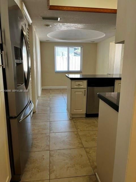 Kitchen featuring a stainless steel refrigerator, tile flooring, built-in cabinetry, dark countertops, and a circular recessed ceiling detail