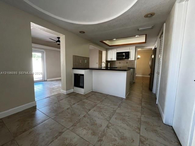 Kitchen featuring a breakfast bar with stone-surfaced countertops, white cabinetry, integrated microwave, tiled backsplash, and neutral ceramic tile flooring