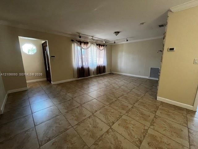 Interior space featuring large-format tile flooring, crown molding, adjustable multi-head track lighting, and a stone-clad feature wall