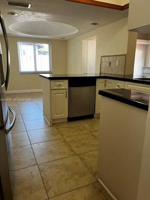 Kitchen featuring white cabinetry, dark countertops, a stainless steel dishwasher, large-format tile flooring, and a circular recessed ceiling fixture
