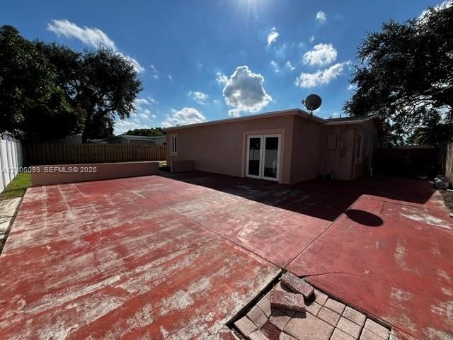 Large concrete patio with low-profile perimeter wall, dual-pane glass French doors, and enclosed yard with wood-style fencing