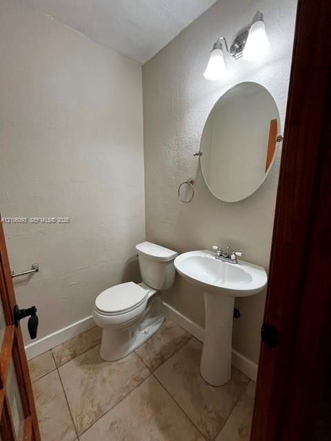 Pedestal sink with dual-handle faucet, oval wall-mounted mirror, ceramic tile flooring, and dual-bulb light fixture