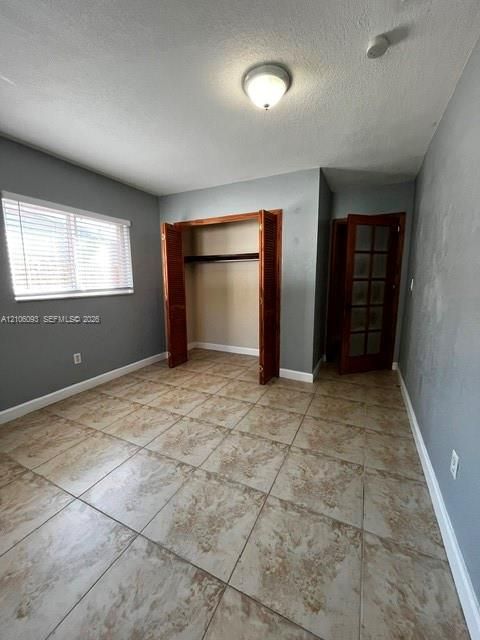 Room featuring large-format stone-patterned tile flooring, multi-pane wood door, closet with louvered wood-finish bifold doors, and window with horizontal blinds