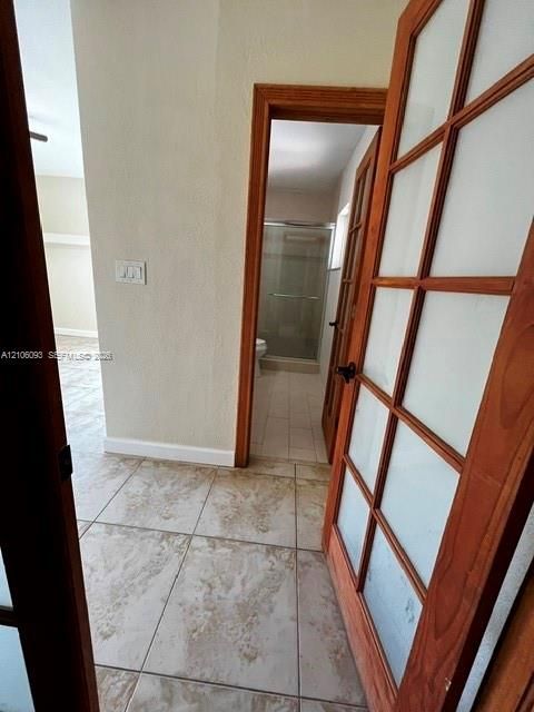 Interior passageway featuring wood-frame French doors with frosted glass panels and neutral-toned tile flooring