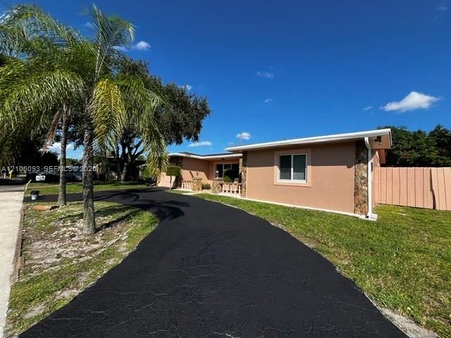 Single-story exterior featuring a stucco finish, stone veneer accents, a paved driveway, and mature palm landscaping