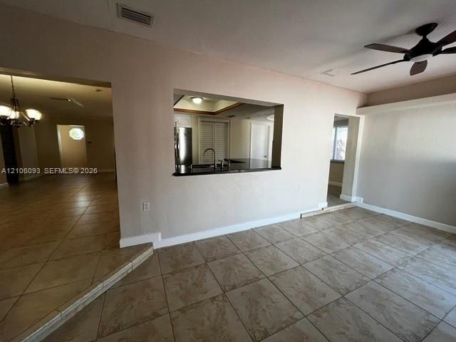 Ceramic tile flooring, pass-through kitchen opening with a dark surface countertop, ceiling fan with light fixture, and chandelier lighting