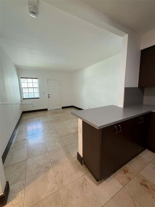 Kitchen area featuring dark cabinetry, solid-surface countertops, large-format tile flooring, and a multi-pane window