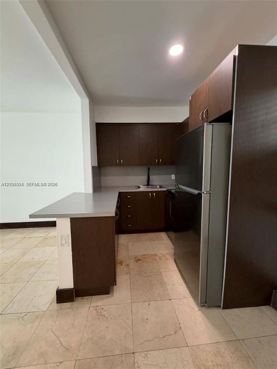 Kitchen featuring dark wood-finish cabinetry, solid-surface countertops, stone-finish flooring, and a stainless steel refrigerator
