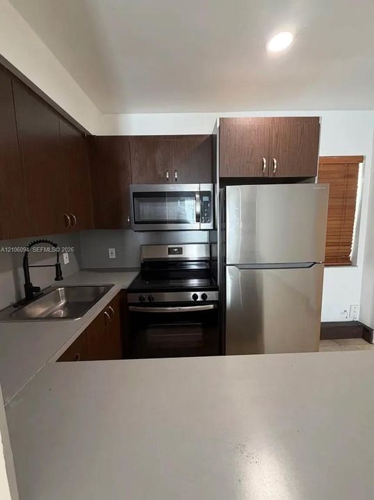 Kitchen featuring wood-finish cabinetry, stainless steel appliances, a matte black faucet, and solid-surface countertops