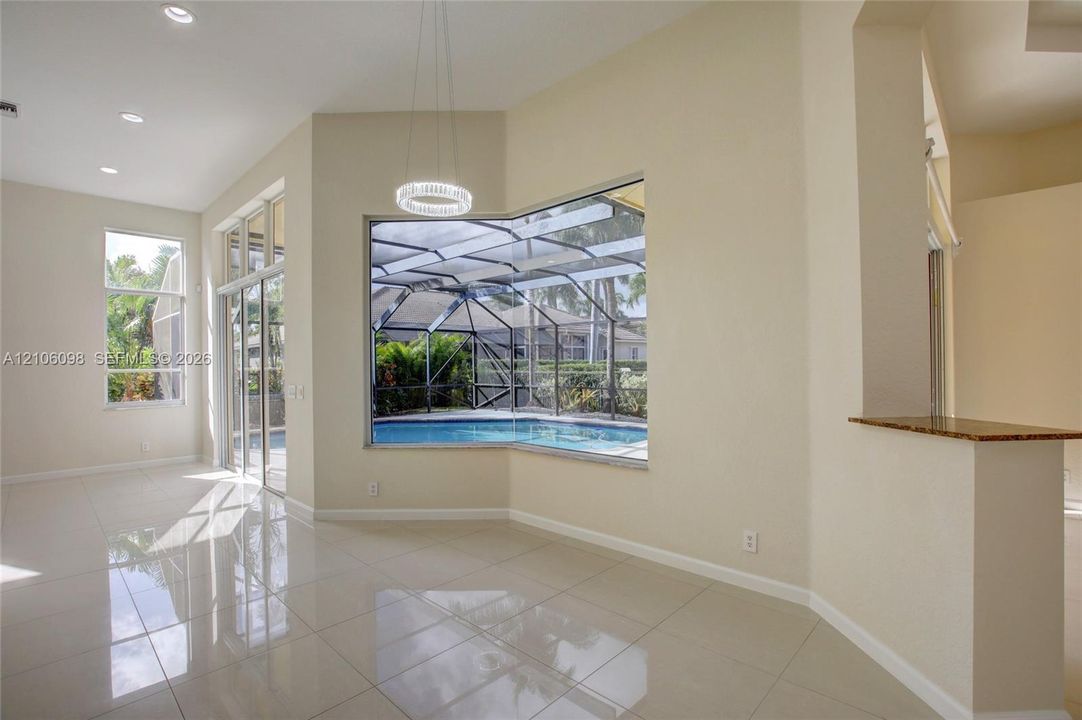 Open-concept interior featuring polished tile flooring, recessed lighting, a built-in stone-surface counter, and large windows encompassing a screened-in pool enclosure