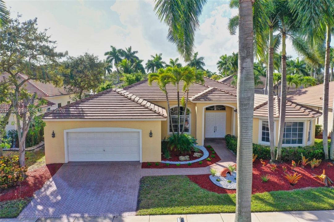 Stucco exterior featuring a tiled roof, multi-pane arched windows, a paved driveway, and mature palm trees