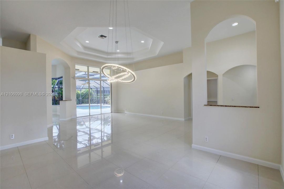 Octagonal tray ceiling, polished tile flooring, contemporary circular chandelier, arched wall cutouts, and expansive sliding glass doors