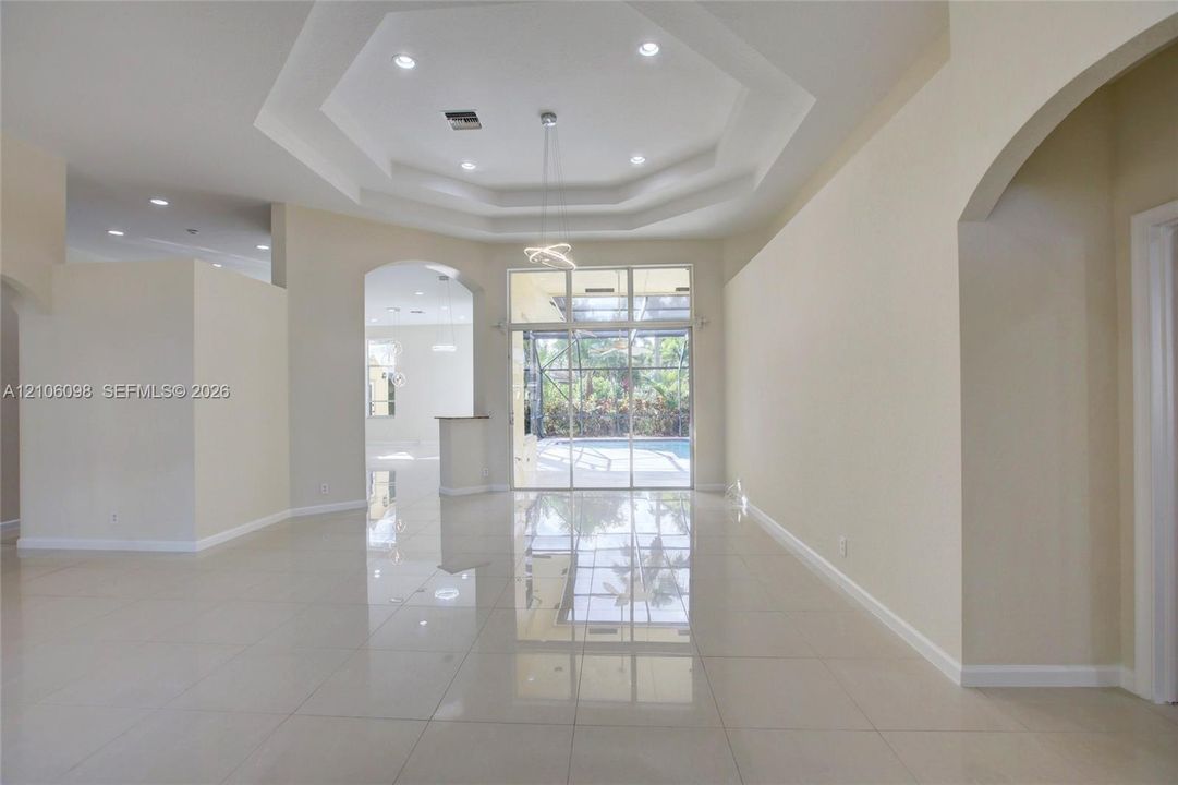 Open interior featuring polished tile flooring, tray ceilings with recessed lighting, an architectural archway, and expansive floor-to-ceiling glass panel doors