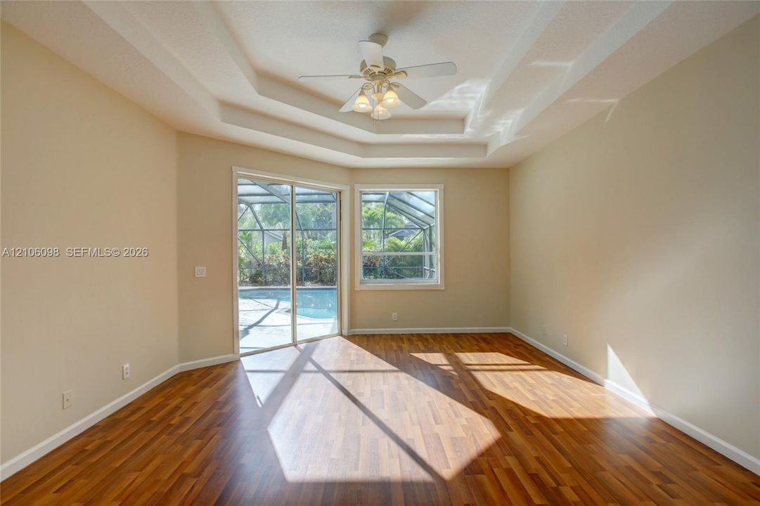 Room featuring tray ceilings, wood-finish flooring, a ceiling fan with integrated lighting, and sliding glass doors with access to a screened-in pool enclosure