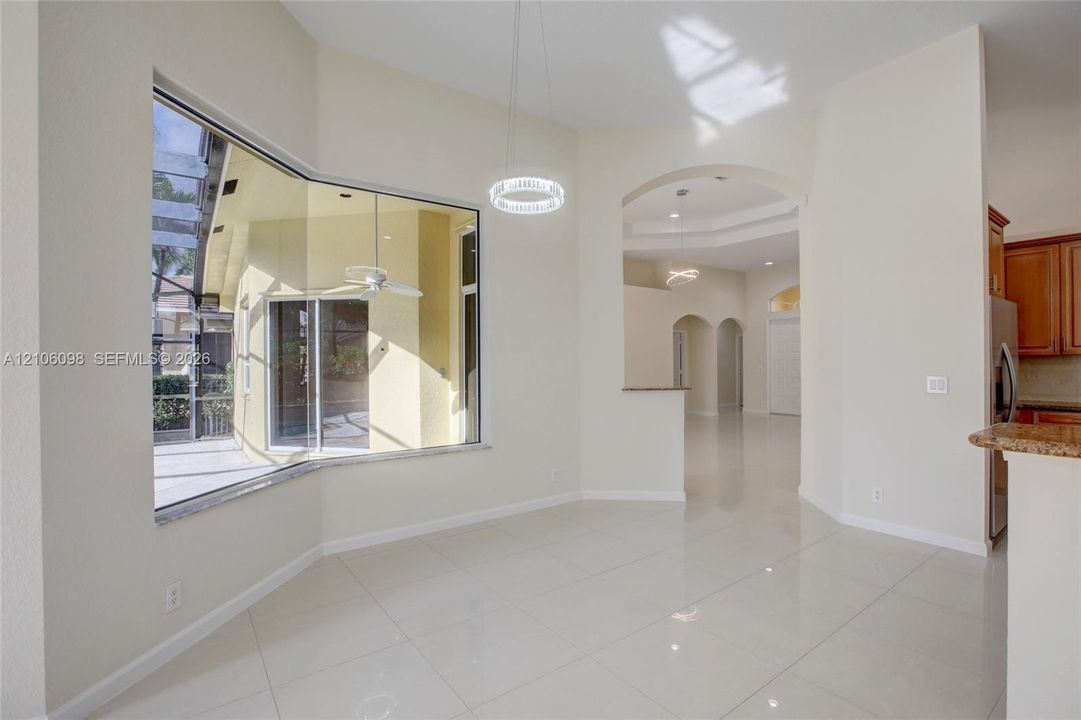 Large bay window, polished tile flooring, arched architectural openings, circular LED pendant lighting, and stone-surfaced breakfast bar