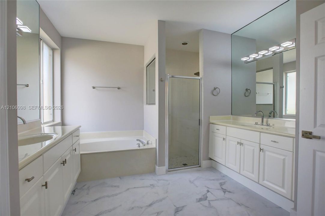 Bathroom featuring dual white vanities with surface-mounted sinks, a built-in soaking tub, a glass-enclosed shower, and large-format flooring