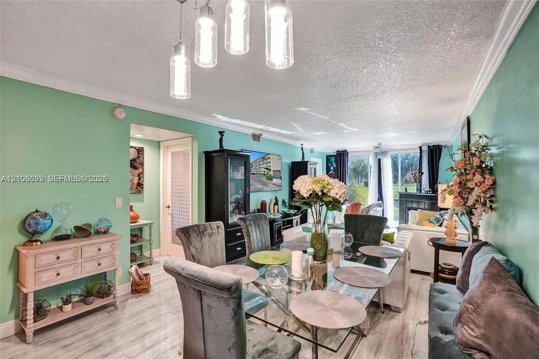 Living area featuring wood-finish tile flooring, crown molding, multi-pendant glass lighting, and sliding glass doors