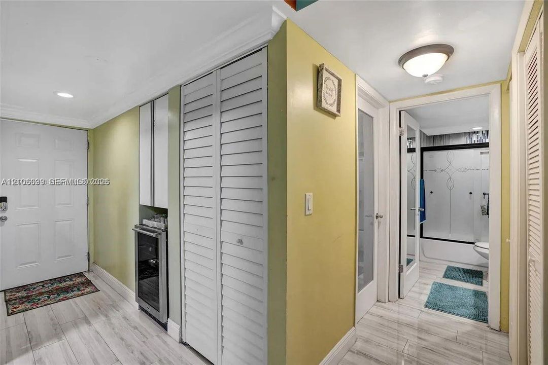 Interior hallway featuring wood-finish flooring, built-in beverage refrigerator with cabinetry, louvered closet doors, and recessed ceiling lighting
