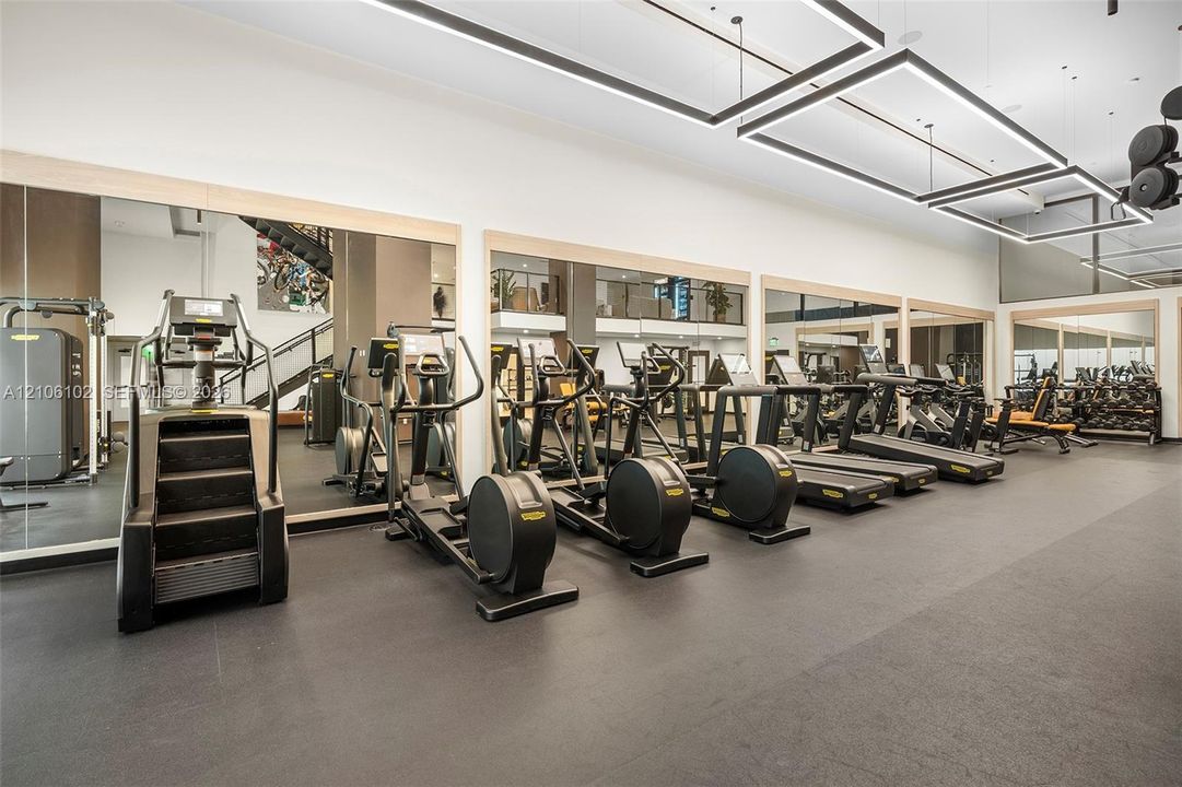 Fitness room featuring wall-to-wall mirrors, recessed square LED lighting fixtures, and high-durability rubber flooring