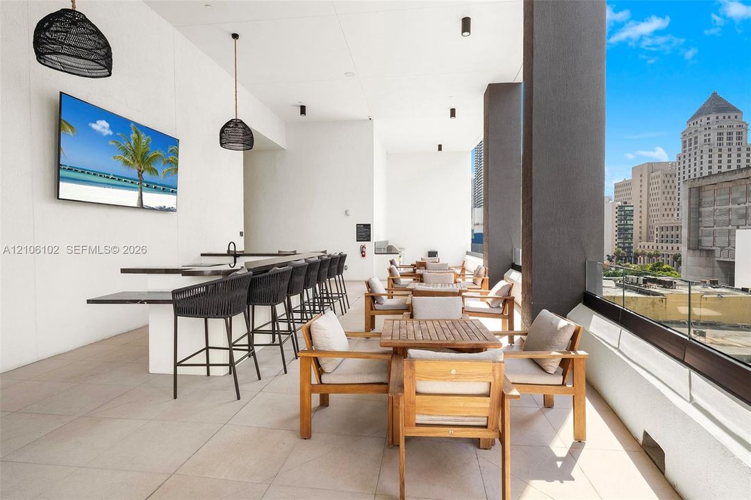 Covered terrace featuring large-format tile flooring, a built-in bar with stone countertop, dark pendant lighting, and glass-paneled railing