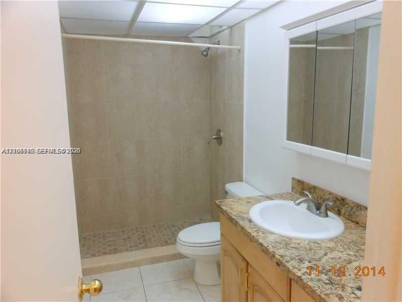 Bathroom featuring a walk-in shower with tile surround, stone-finish vanity countertop with an integrated basin, mirrored medicine cabinet, and tile flooring